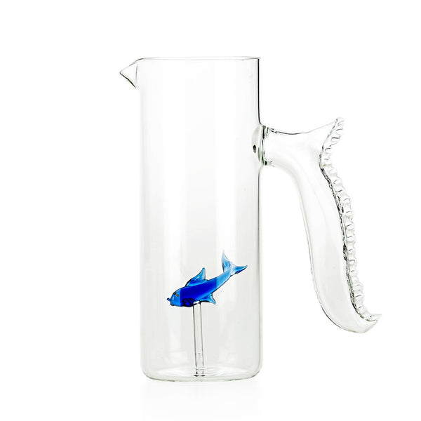 A transparent Murano glass jug with a blue fish-shaped handle and a red fish-shaped detail emerging from the jug.