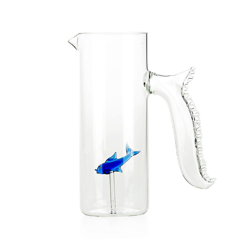 A transparent Murano glass jug with a blue fish-shaped handle and a red fish-shaped detail emerging from the jug.