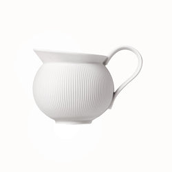 A white porcelain milk jug with vertical ridges and a curved handle, against a white background.