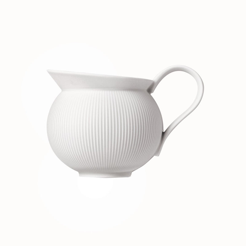 A white porcelain milk jug with vertical ridges and a curved handle, against a white background.