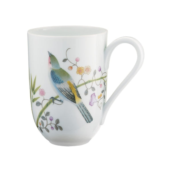 A white porcelain mug with a floral motif and images of birds of paradise, exotic plants, and butterflies.