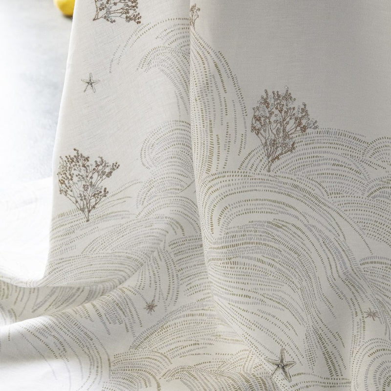 Close-up of a white linen tablecloth with a large-scale embroidered design featuring coral branches, pearls, and starfish, and embroidery in beige and white gold thread.