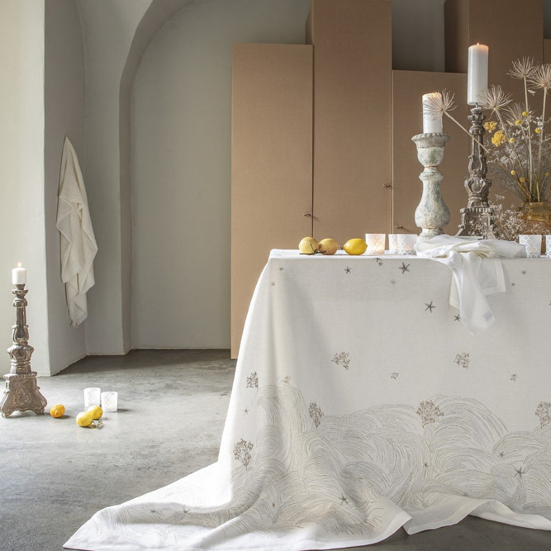 Styled Dining Table with a white tablecloth and big candles on top, with a beige background