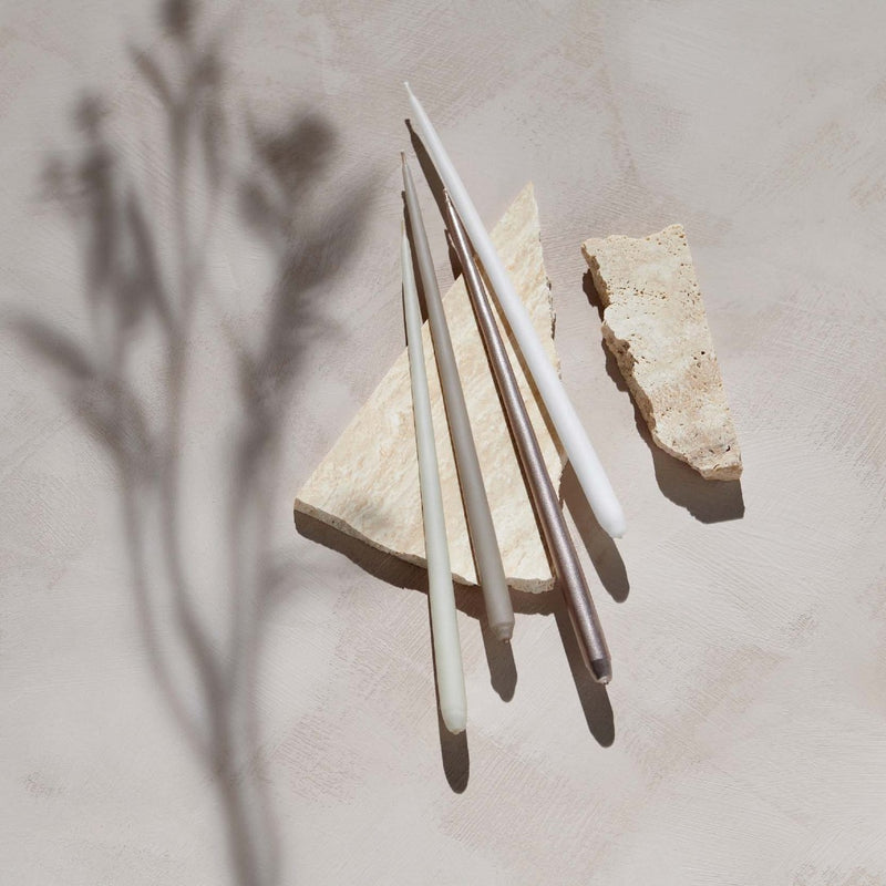4 slim taper candles in white and natural colour agains a textured beige surface
