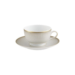 A white porcelain tea cup with gold and black geometric patterns on the cup and saucer, set against a plain background.