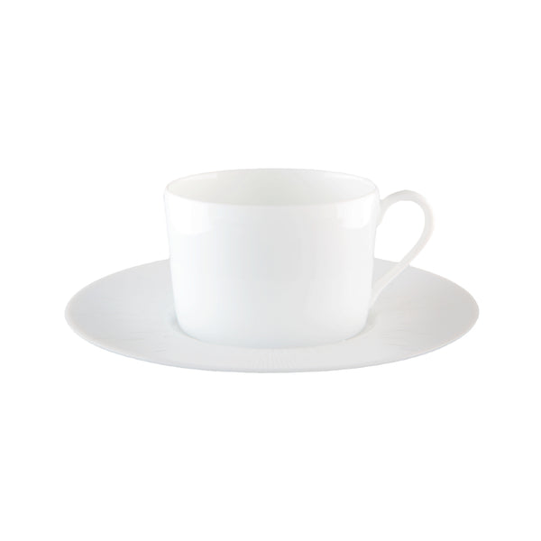 A white porcelain tea cup with a saucer, displaying a counter-relief engraving which is part of the Infini collection by Haviland.
