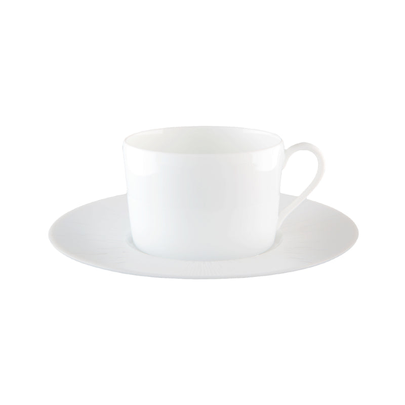 A white porcelain tea cup with a saucer, displaying a counter-relief engraving which is part of the Infini collection by Haviland.