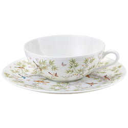 A white porcelain tea cup and saucer with turquoise and brown floral patterns, featuring birds of paradise and exotic plants.
