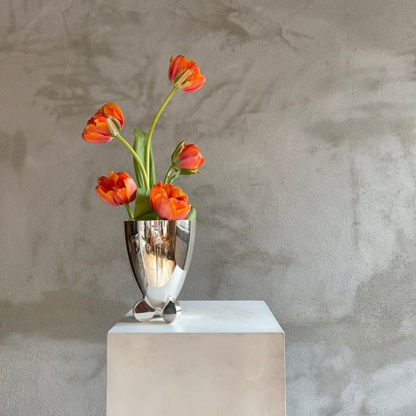 orange tulips in a silver plated vase against a grey textured wall